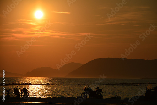 Sunset on the beach. The mountains in the background. In the foreground, silhouettes of motorcycles. 
