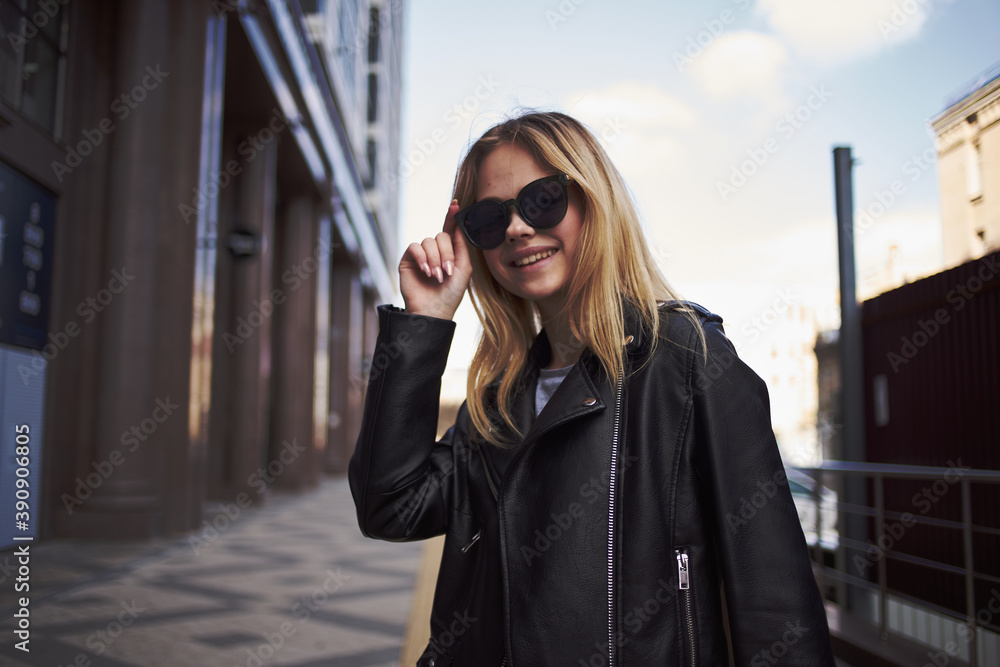 Fashionable woman in a leather jacket and sunglasses near the building on the street