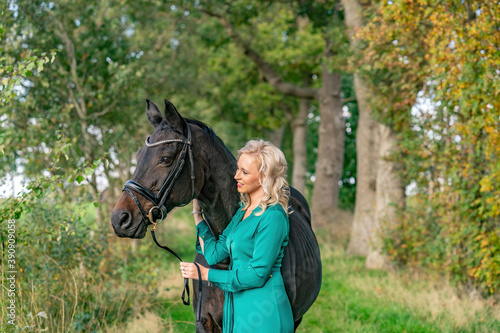 Happy beautiful blond girl in a green dress, cuddling her horse outdoors. Selective focus on the horse, autumn colos. Narrow depth of field, copy-space