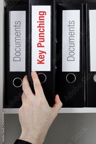 Key Punching. File Folder is taking by a hand from office shelf. Red Text is on the label of the documents. photo