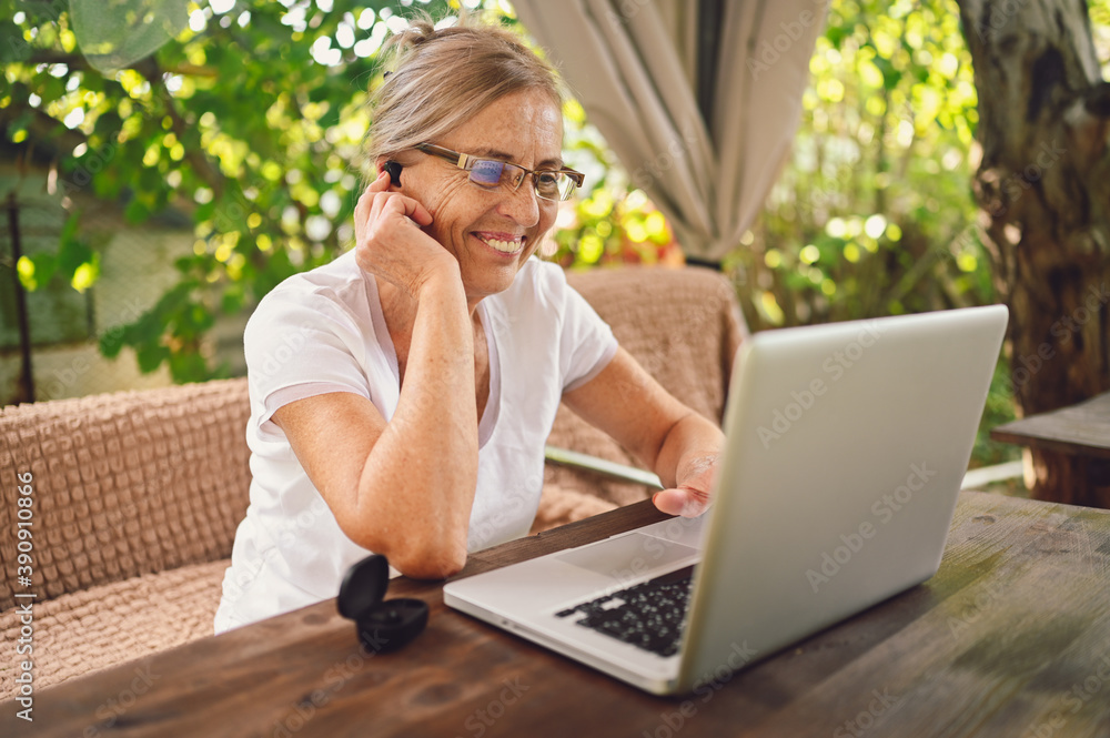 Happy senior woman use wireless headphones working online with laptop computer outdoor in garden Happy senior woman use wireless headphones working online with laptop computer outdoor in garden