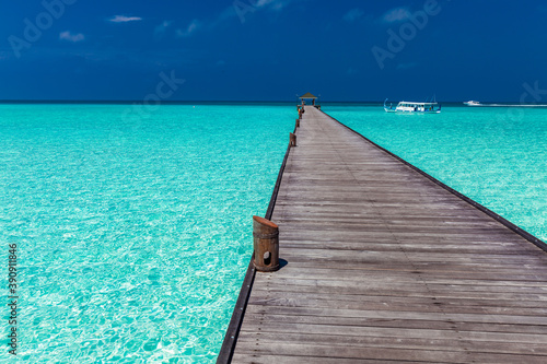 Jetty over atoll and a tropical resort island in Maldives