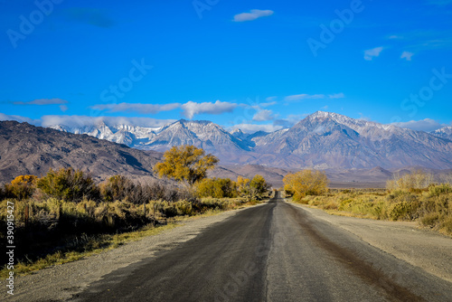 rural road to mountains with autumn trees and snow clouds in blue sky landscape © mariekazalia