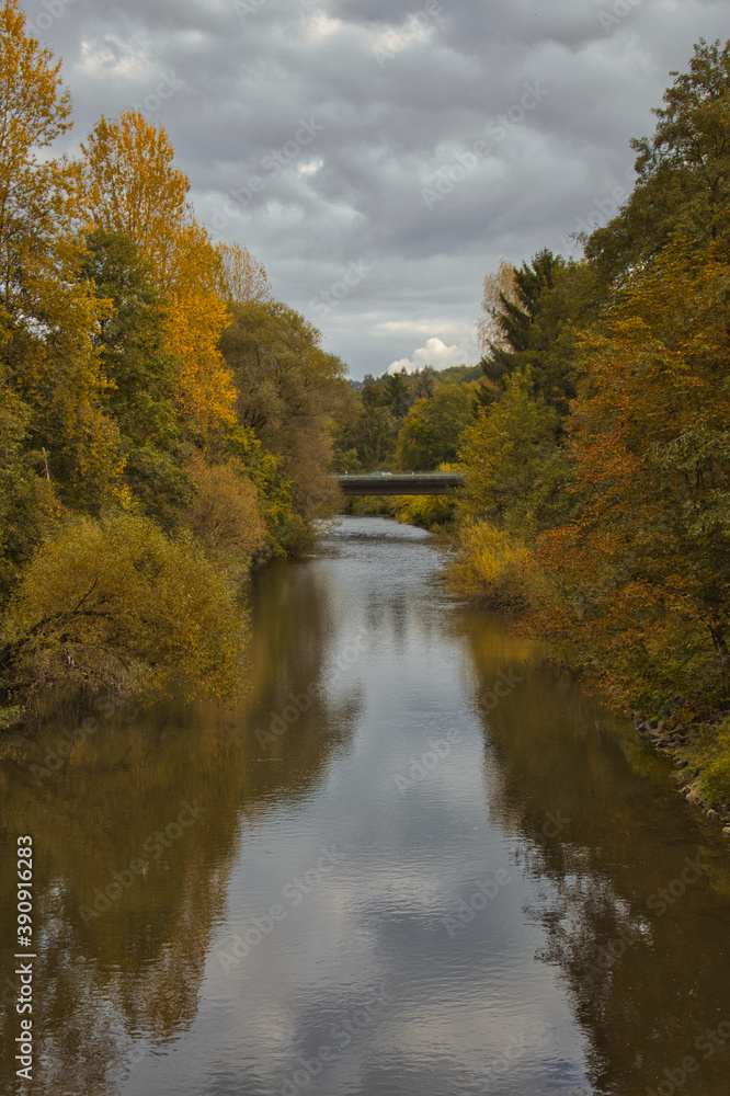 Fototapeta premium Fluss mit Brücke im Hintergrund umrahmt von herbstlichen Bäumen