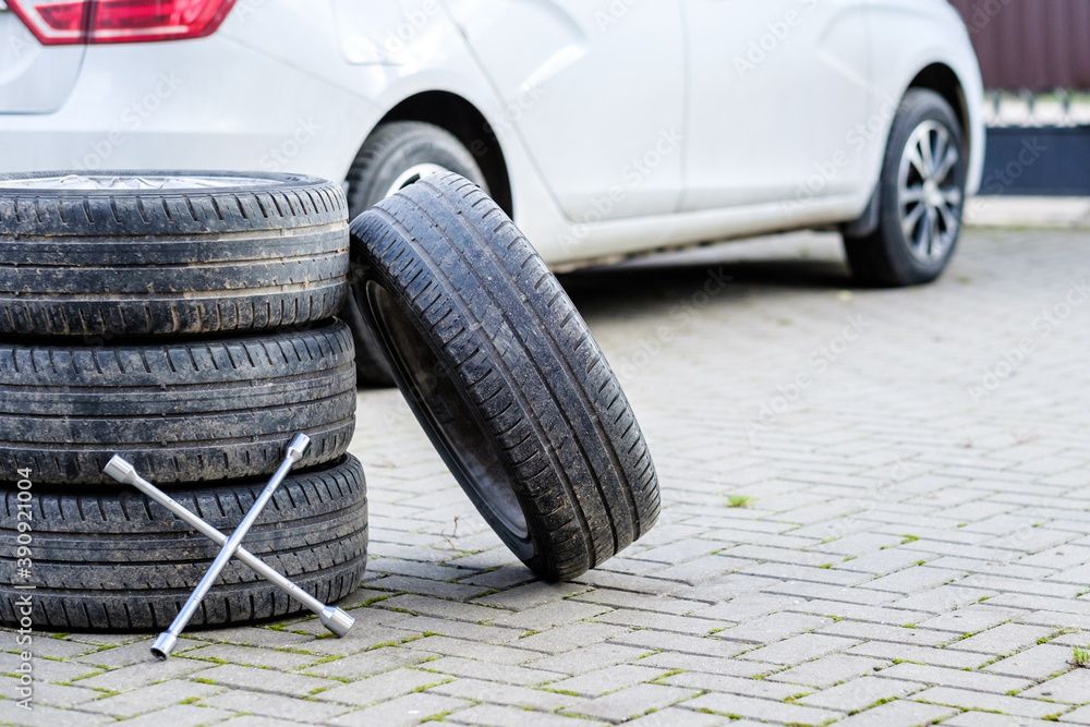 The wrench rests on the foot of the car wheels. An unknown white car on a blurred background. The concept of seasonal replacement of summer car tires with winter tires. Autumn day. The wrench rests on the foot of the car wheels. An unknown white car on a blurred background. The concept of seasonal replacement of summer car tires with winter tires. Autumn day.