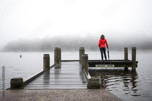 Woman in red from behind overlooking misty fogy view after hike walk outdoors on overcast day
