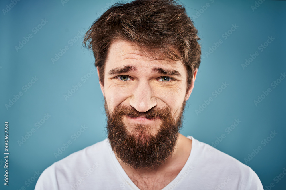 Fototapeta premium Bearded man displeased facial expression emotions close-up blue background white t-shirt