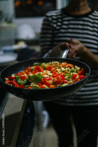 Unrecognizable woman holds frying pan with sauteed vegetables for Mexican food recipe. Bring peppers and onions.