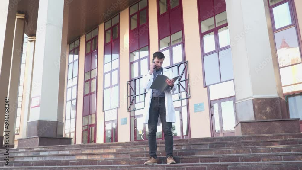 Doctor reading medical documents while talking on phone near his office. Medicine, people and healthcare concept. Male physician makes phone call regarding medical report. Doc checking medical record Doctor reading medical documents while talking on phone near his office. Medicine, people and healthcare concept. Male physician makes phone call regarding medical report. Doc checking medical record