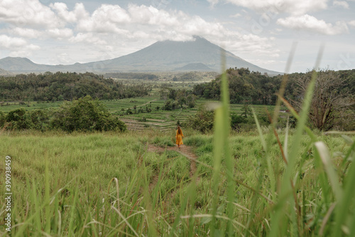 Back view young girl in yellow dress walking in rice field in Bali with view on famous volcano Agung. Trevelling to clean places of Earth and discovering beauty of nature photo