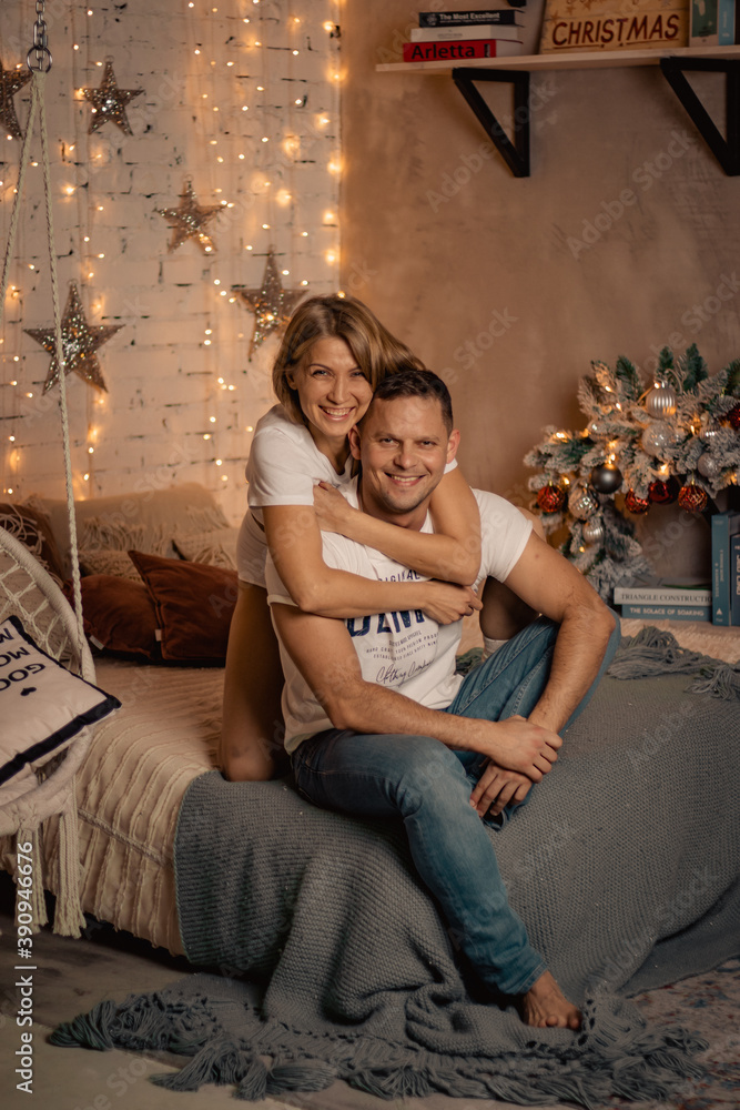 Obraz premium Romantic christmas evening of young couple. New year love story. Photo session of lovers in the studio. Christmas decorated room, new year atmosphere.
