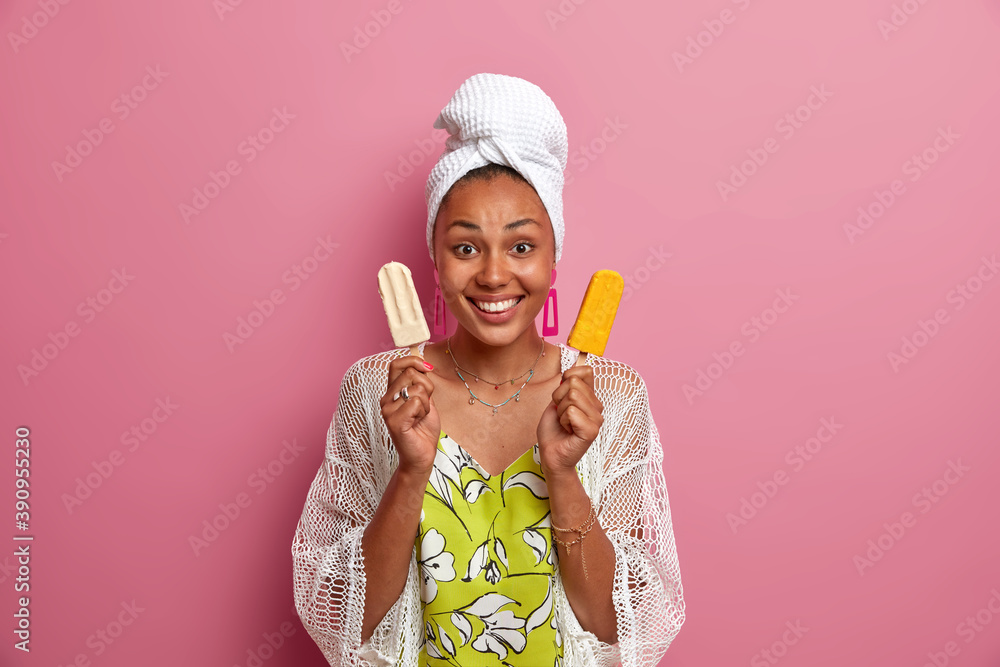 Indoor shot of glad healthy woman with pure clean skin after taking shower smiles broadly has white perfect teeth holds two delicious ice creams isolated over pink background. Summer dessert Indoor shot of glad healthy woman with pure clean skin after taking shower smiles broadly has white perfect teeth holds two delicious ice creams isolated over pink background. Summer dessert