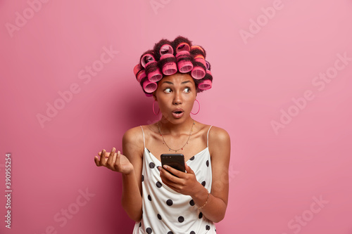 Принти на полотні Beautiful embarrassed surprised dark skinned Afro American woman holds mobile ph