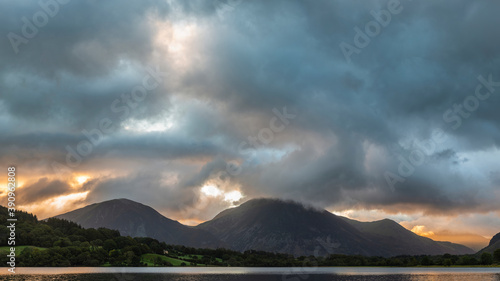 Beautiful sunrise landscape image looking across Loweswater in the Lake District towards Low Fell and Grasmere with vibrant sunrise sky breaking on the mountain peaks