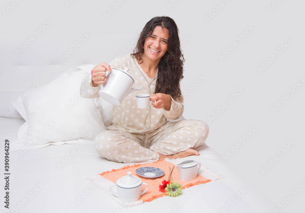 Spanish attractive brunette woman sitting on a bed having a cup of coffee or tea