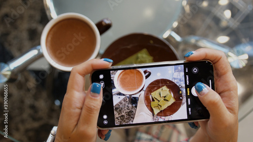 Close up of woman holds modern smartphone and taking pictures of her morning breakfast cocoa and green chocolate to share photos on social media resources