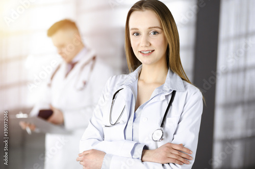 Professional beautiful woman-doctor with a stethoscope is standing with crossed arms in a sunny clinic. Young doctors at work in a hospital. Medicine and healthcare concept