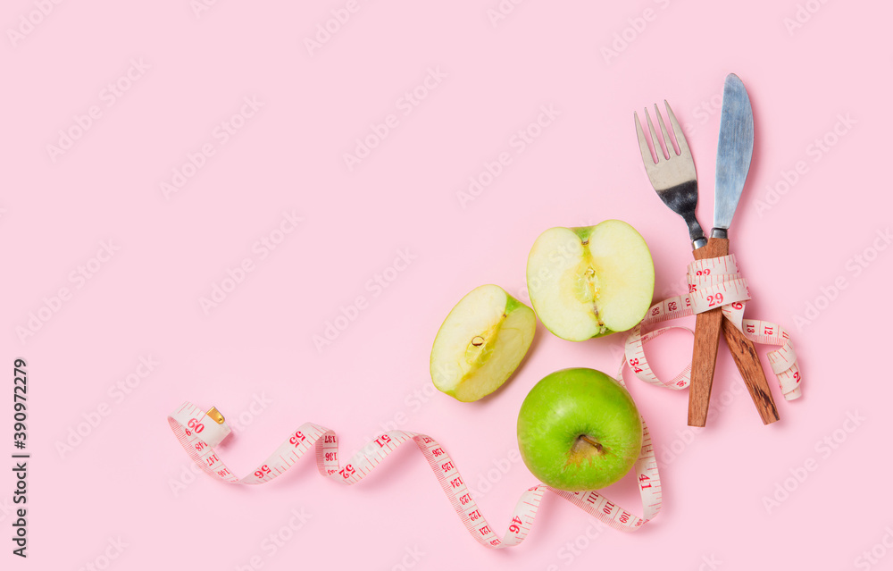 Green apple with measuring tape around fork and knife isolated on pink background, Green apple with measuring tape around fork and knife isolated on pink background,