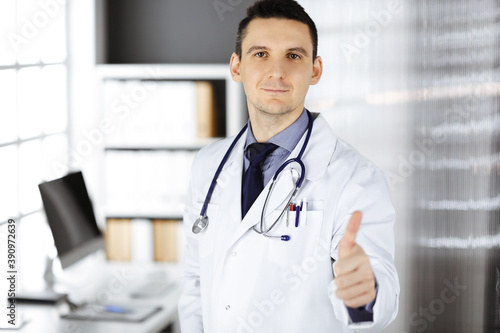 Male doctor standing with thumbs up sign in clinic near his working place. Perfect medical service in hospital. Medicine and healthcare concept