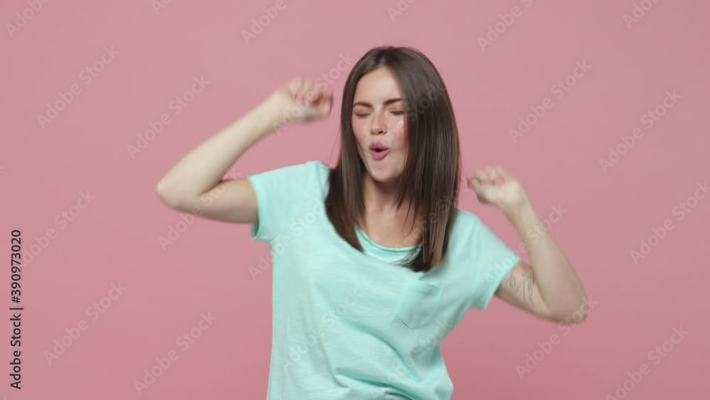 Cheerful funny young brunette woman 20s years old in blue t-shirt posing isolated on pastel pink background studio. People lifestyle concept. Looking camera dancing showing victory sign waving hands Cheerful funny young brunette woman 20s years old in blue t-shirt posing isolated on pastel pink background studio. People lifestyle concept. Looking camera dancing showing victory sign waving hands