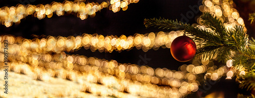 Canvas-taulu Red Christmas bauble on a conifer branch with fairy lights in the background bok