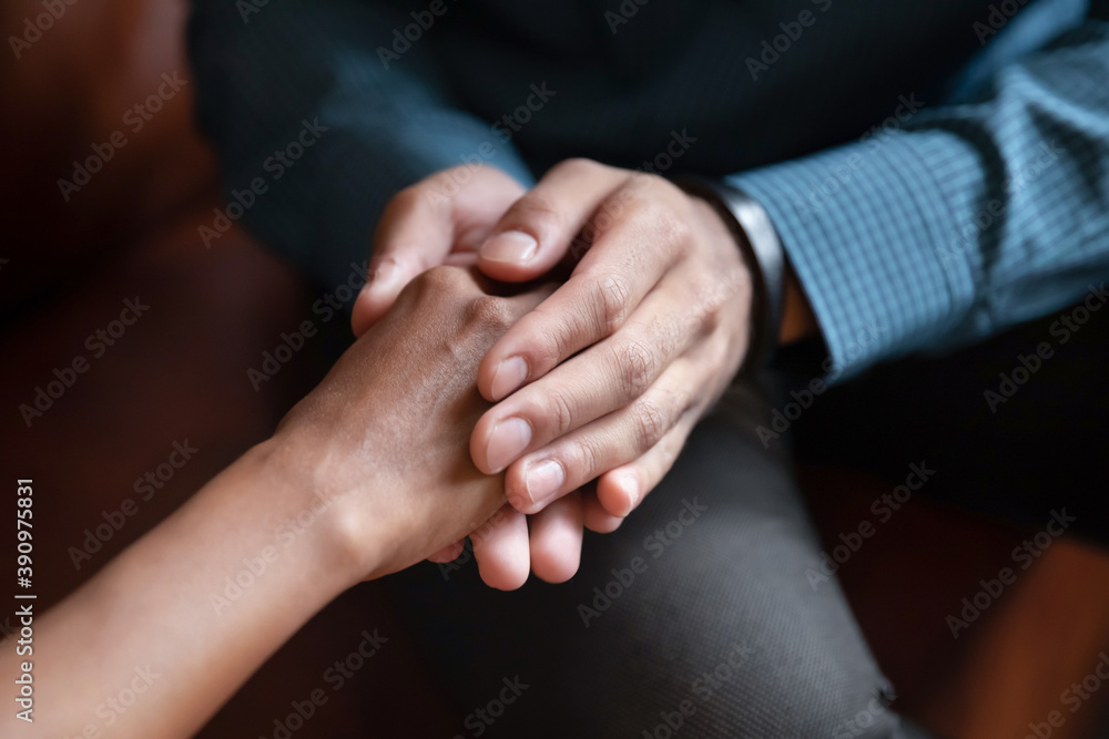 Hand in hands. Close up of young man husband boyfriend holding hand of beloved mixed race woman wife girlfriend comforting supporting in grief, asking forgiveness, apologizing after family argument