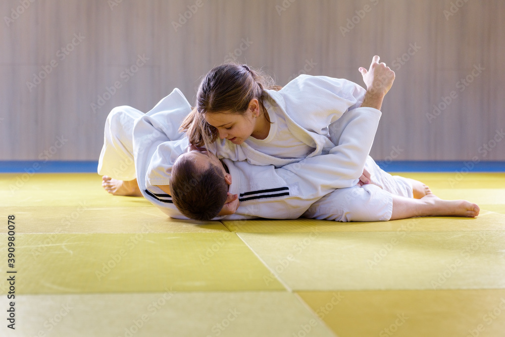 Young female judoka holds older male judoka with kesa gatame technique