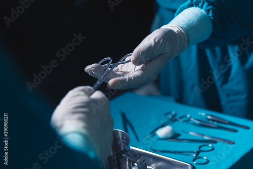 Two surgeons working in operating room, one hand over surgical equipment to another. Surgeons hands holding surgical scissors and passing surgical equipment, close-up. 