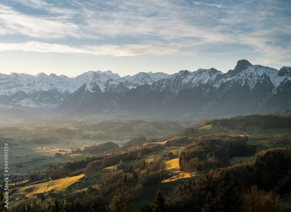 overview swiss landscape with hills forests mountains in warm color during sunset or sunrise and epic sky