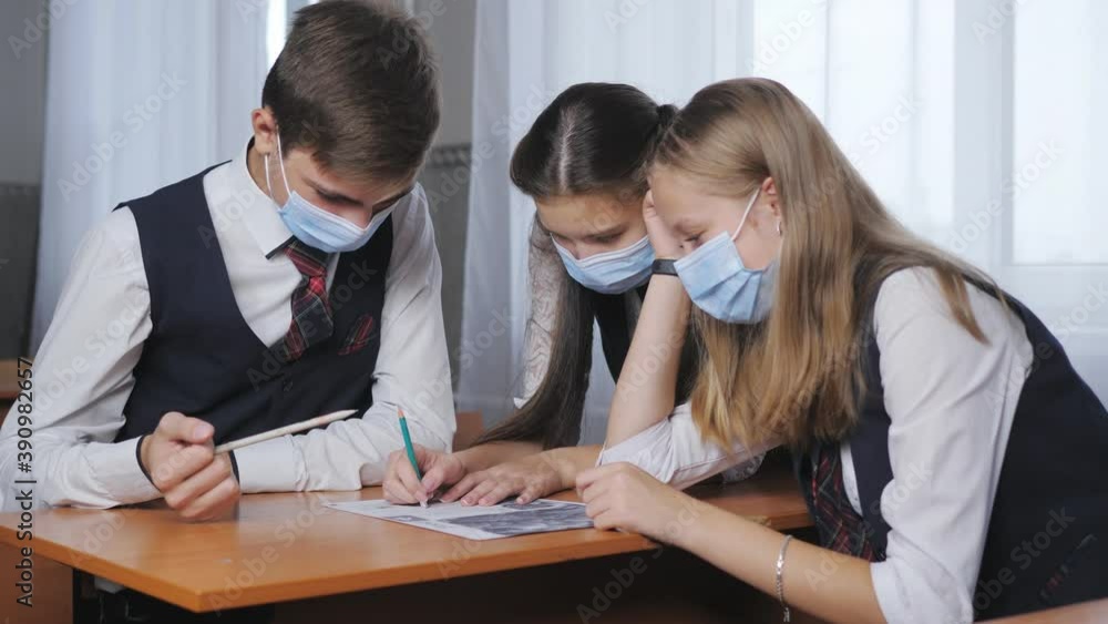 Students in medical masks sit in the classroom and deal with the task of the teacher. Students in medical masks sit in the classroom and deal with the task of the teacher.