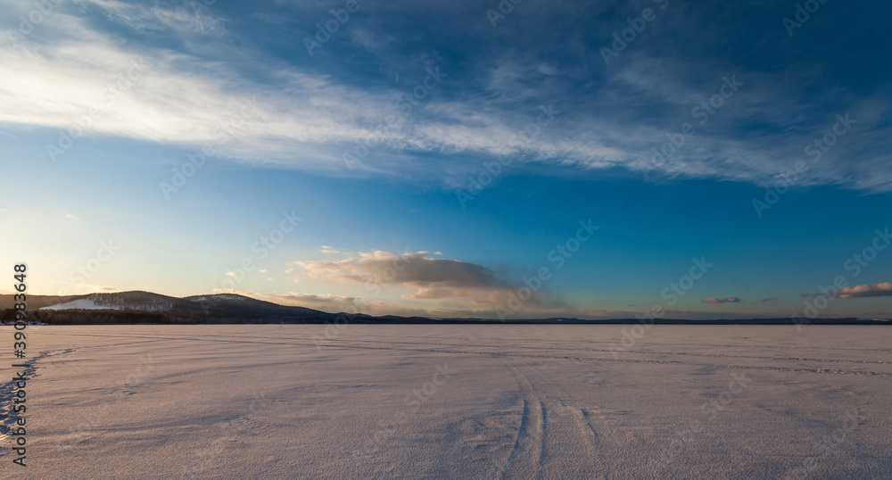 frozen lake in winter on a background of blue sky with clouds