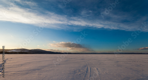 frozen lake in winter on a background of blue sky with clouds