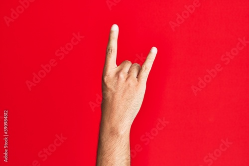 Arm of caucasian white young man over red isolated background gesturing rock and roll symbol, showing obscene horns gesture photo