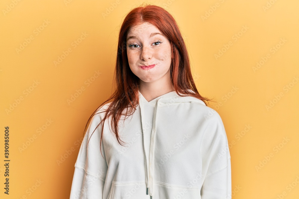 Young red head girl wearing casual sweatshirt puffing cheeks with funny face. mouth inflated with air, crazy expression. Young red head girl wearing casual sweatshirt puffing cheeks with funny face. mouth inflated with air, crazy expression.