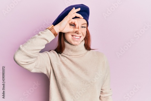 Young red head girl wearing french look with beret smiling happy doing ok sign with hand on eye looking through fingers © Krakenimages.com