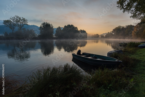 Calm scenic picture of small fishing boat on the Adda river on a hazy sunrise