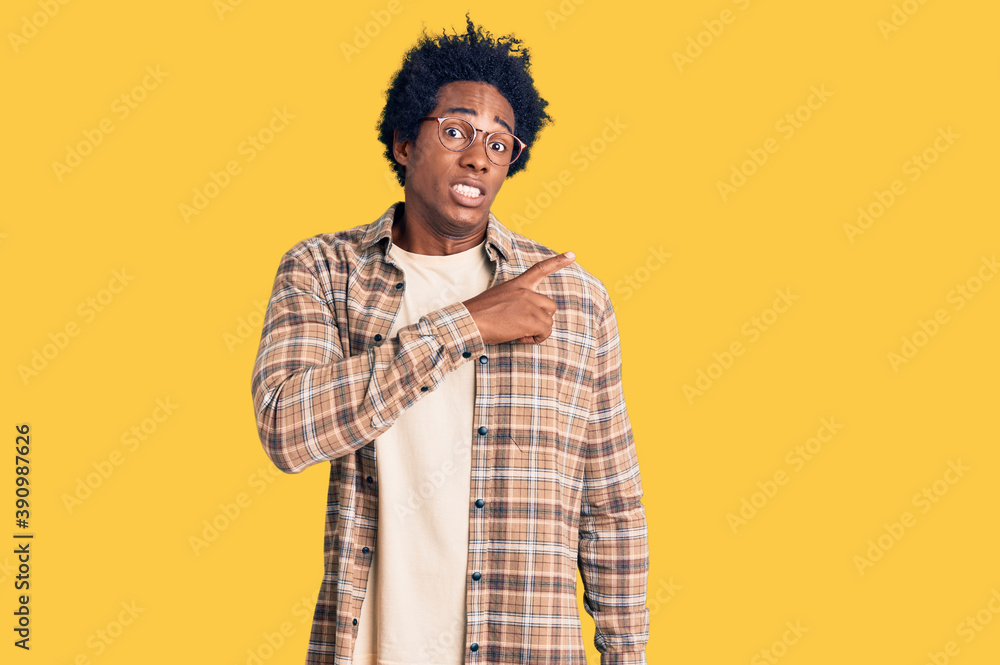 Handsome african american man with afro hair wearing casual clothes and glasses pointing aside worried and nervous with forefinger, concerned and surprised expression Handsome african american man with afro hair wearing casual clothes and glasses pointing aside worried and nervous with forefinger, concerned and surprised expression