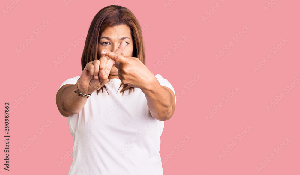 Middle age latin woman wearing casual white tshirt rejection expression crossing fingers doing negative sign Middle age latin woman wearing casual white tshirt rejection expression crossing fingers doing negative sign