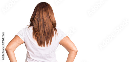 Middle age latin woman wearing casual white tshirt standing backwards looking away with arms on body