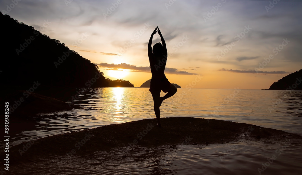 Silhouette of sportwoman practicing yoga on the beach with sunset sky scene