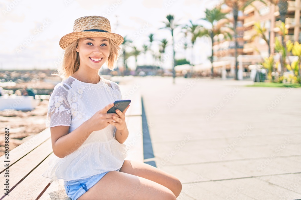 Fototapeta premium Young caucasian tourist girl smiling happy using smartphone sitting on bench at promenade.
