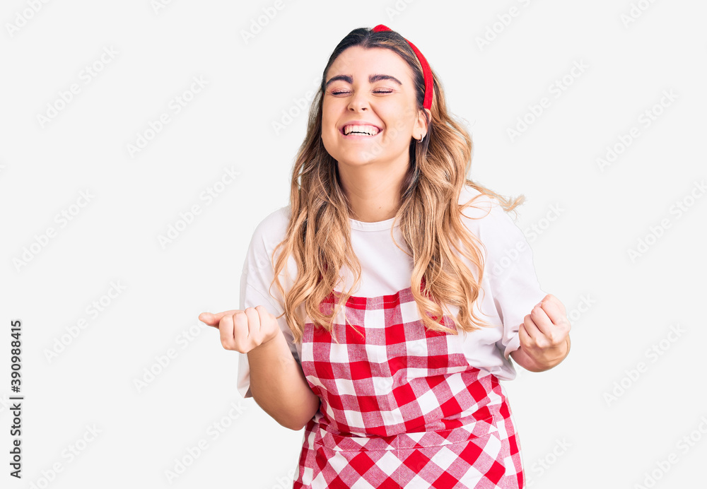 Young caucasian woman wearing apron very happy and excited doing winner gesture with arms raised, smiling and screaming for success. celebration concept. Young caucasian woman wearing apron very happy and excited doing winner gesture with arms raised, smiling and screaming for success. celebration concept.