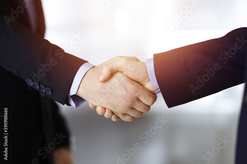 Business people shaking hands, close-up. Group of unknown businessmen standing in a sunny modern office. Teamwork, partnership and handshake concept