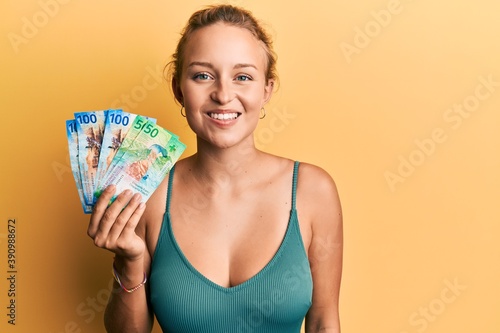 Beautiful caucasian woman holding swiss franc banknotes looking positive and happy standing and smiling with a confident smile showing teeth