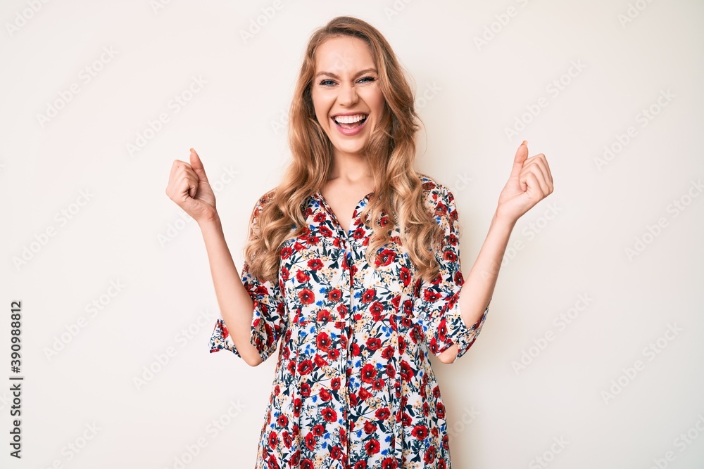 Young caucasian woman with blond hair wearing summer dress celebrating surprised and amazed for success with arms raised and open eyes. winner concept. Young caucasian woman with blond hair wearing summer dress celebrating surprised and amazed for success with arms raised and open eyes. winner concept.