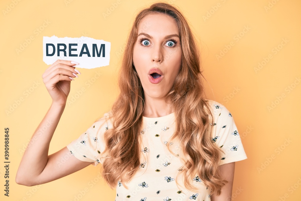Young caucasian woman with blond hair holding dream word paper scared and amazed with open mouth for surprise, disbelief face Young caucasian woman with blond hair holding dream word paper scared and amazed with open mouth for surprise, disbelief face