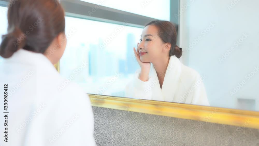 Young happy asian woman in front of a bathroom mirror touching smooth face skin. Skincare cosmetics and makeup concept, full frame slow motion Young happy asian woman in front of a bathroom mirror touching smooth face skin. Skincare cosmetics and makeup concept, full frame slow motion