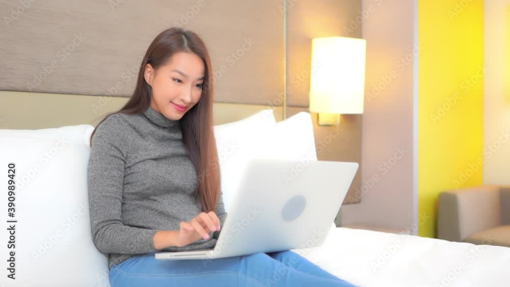 In a work from anywhere culture, a young woman relaxes on a big comfortable bed as she works on her laptop. In a work from anywhere culture, a young woman relaxes on a big comfortable bed as she works on her laptop.