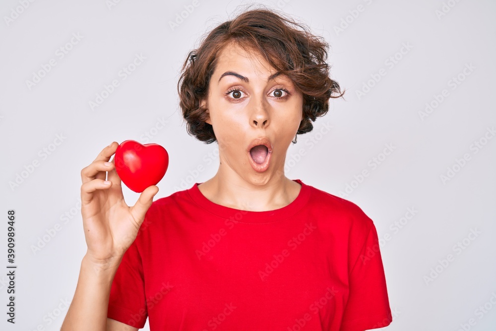 Young hispanic woman holding heart scared and amazed with open mouth for surprise, disbelief face Young hispanic woman holding heart scared and amazed with open mouth for surprise, disbelief face