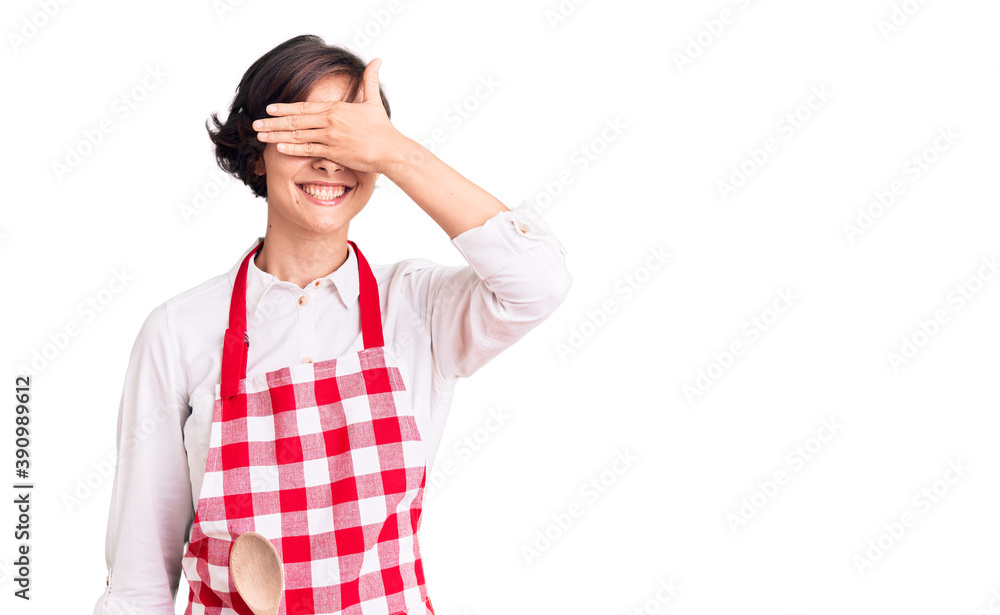 Beautiful young woman with short hair wearing professional cook apron smiling and laughing with hand on face covering eyes for surprise. blind concept. Beautiful young woman with short hair wearing professional cook apron smiling and laughing with hand on face covering eyes for surprise. blind concept.